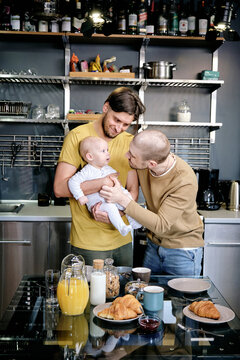 Two cheerful gay men playing with baby boy in the kitchen