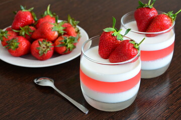 strawberry jelly dessert in the glasses decorated with strawberry and plate with strawberries and teaspoon on the wooden kitchen table