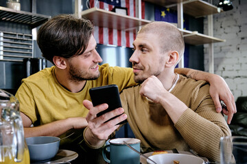 Young male embracing his boyfriend during talk by breakfast