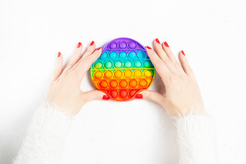 Female hands with red manicure squeeze silicone flexible anti-stress pop it or simple dimple on white background