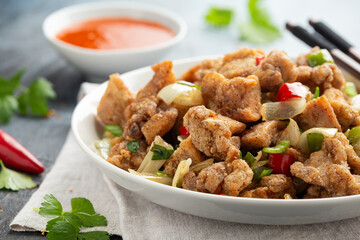 Stir fry chinese salt and pepper chicken with red, green chilli, onion, spring onion in white bowl.