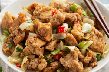 Stir fry chinese salt and pepper chicken with red, green chilli, onion, spring onion in white bowl.