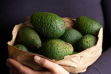 Woman holding paper carrier bags, full of fresh avocado. Healthy food.