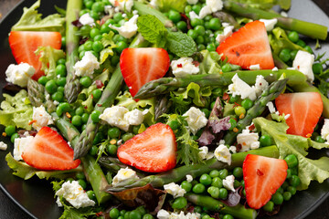 Asparagus and Strawberry Salad with vegetables, green peas and feta cheese in black plate. healthy...