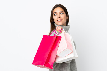 Fototapeta na wymiar Young caucasian woman isolated on white background holding shopping bags and looking back