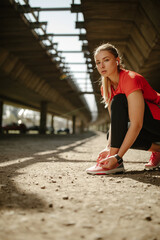 A blonde fit girl ties her sneakers and prepares to run.