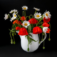 bouquet of daisies and poppies in a vase on a black background, rays of light