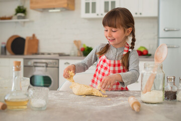 Cute little 4 year old girl with pigtails rolls out dough with a rolling pin on the kitchen table