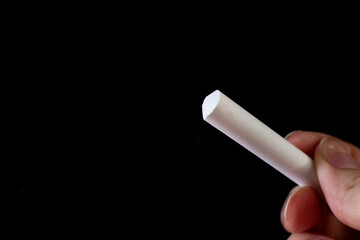Close up of a hand holding a piece of white chalk.