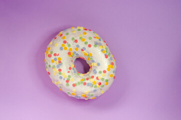 Donut in white glaze and round multi-colored balls on an lilac background