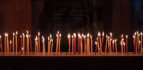 A line of burning yellow candles at the dark church background.