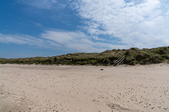 wooden stairs lead over tall grassy sand dunes onto an empty picturesque golden sand beach - Powered by Adobe