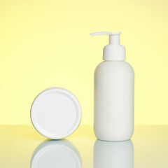 Hand cream in a bottle and jar on a yellow background with reflection.