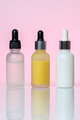 Three bottles of serum on a light pink background. Moisturizer, vitamin C, hyaluronic acid.