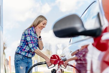 Pretty, smiling woman filling her car with petrol at gas station.
