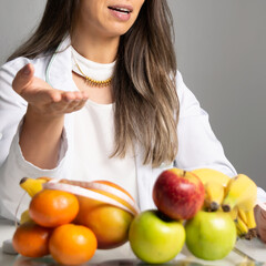 Smiling female nutritionist in her office,  showing healthy vegetables and fruits. Healthcare and diet concept. Lifestyle.