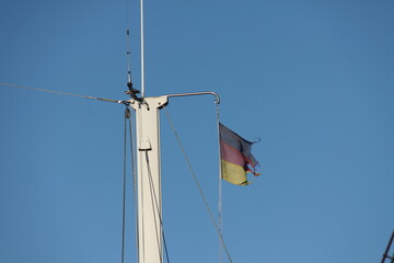 Obraz premium Zerfetzte Deutschlandflagge an Schiffsmast vor blauem Himmel