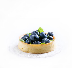 Blueberry tart with mint leaves at white background, side view.
