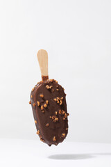 Flying ice cream with chocolate coating and hazelnuts isolated on white background, ice cream popsicle with wooden stick