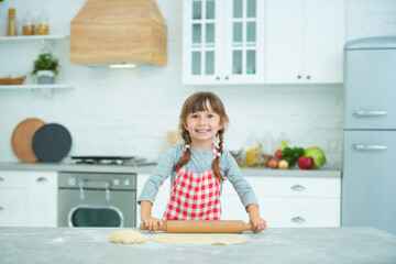 A cute little girl with pigtails in a plaid apron kneads pizza dough on her own. Cooking classes for children