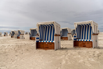 colorful beach baskets on an idyllic golden sand beach on the German Wadden Sea coast under an expressive sky