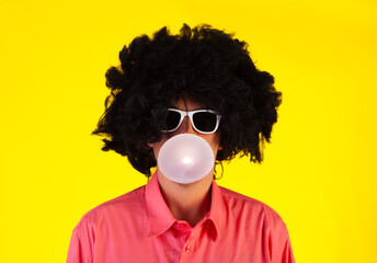 Curly man wearing sunglasses blowing bubble with chewing gum