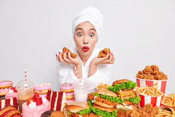 Photo of surprised woman wears red lipstick holds nuggets poses near table full of fast food and...