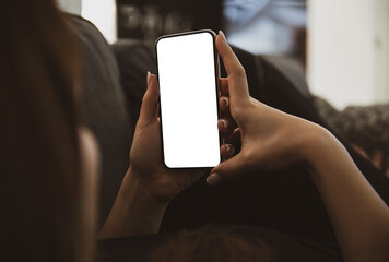 Girl using smartphone blank screen frameless modern design while lying on the sofa in home interior
