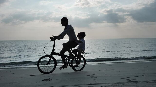Asian family On Summer Vacation Father and son riding bicycles on beach. Relaxation Holiday and Travel concept. Silhouette Slow Motion