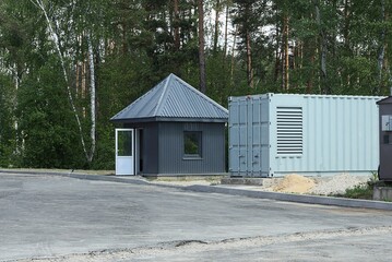 black iron house for security with an open door and window near a gray metal container on the street on the asphalt near the trees