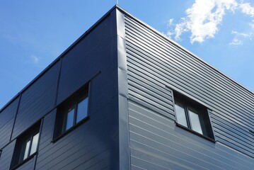 corner of a large house made of black metal with windows against a blue sky