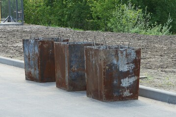 a row of three old iron open trash cans in brown rust stand outside on gray asphalt