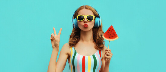 Summer fashion portrait of young woman in headphones listening to music with juicy slice of watermelon, female model blowing her lips posing on a colorful blue background - obrazy, fototapety, plakaty