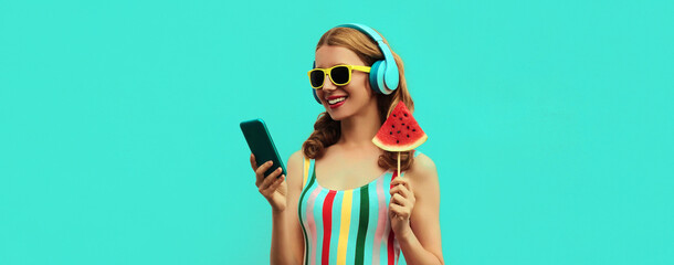 Summer portrait of happy smiling young woman in headphones listening to music on smartphone with...