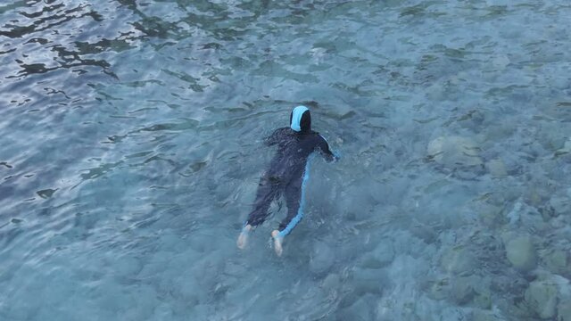 A high angle view of a Muslim woman in burkini swimming in turquoise sea.