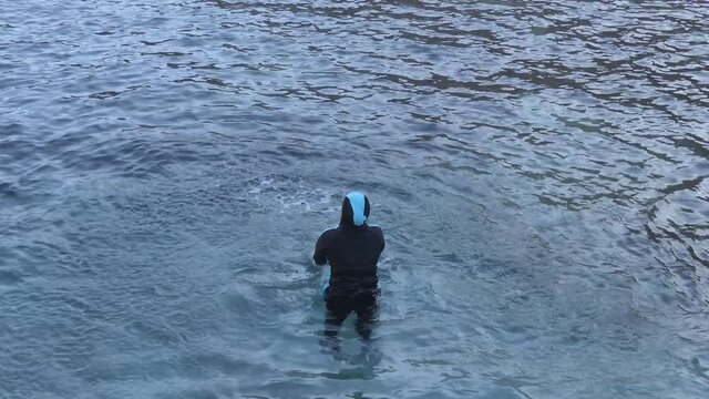 A Muslim woman in burkini splashing water in the sea.