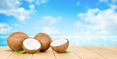Fototapeta na wymiar two whole coconuts and two halves lying on a wooden table against the background of the defocus sea