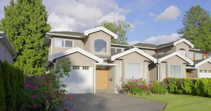 Establishing shot of two story stucco luxury house with garage door, big tree and nice landscape in Vancouver, Canada, North America. Day time on May 2021. ProRes 422 HQ.