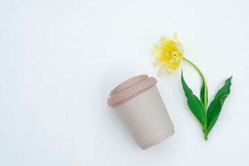 Reusable plastic coffee cup. A travel mug with a splash-proof lid puts away a portable and lightweight drinking flask. Eco-cup with coffee. There are tulips nearby.