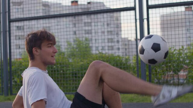 Young Caucasian Amateur Man Practicing Soccer Skills And Tricks With The Football Ball At Sunset In An Playground. Urban City Lifestyle Outdoors Concept. 4K UHD Slow Motion RAW Graded Footage