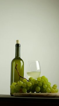 Glass of white wine with bottle and bunch of grapes, still life with copy space, vertical 4k video.
