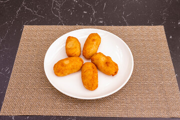 ration of croquettes battered with bread and egg, stuffed with béchamel and serrano ham on a plastic tablecloth
