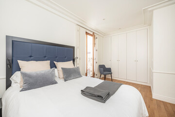 Bedroom with blue and white tones with a built-in wardrobe in the background and a blue slip-on chair