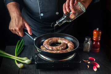 Chef adds oil to pan with raw homemade meat sausage. Preparation for cooking sausages in the kitchen of a restaurant or cafe on table with vegetables