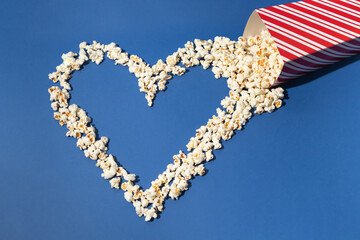 Popcorn falling out of the box and forming heart shape on royal blue background, interesting concept, modern flat lay style.