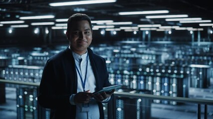Handsome Smiling IT Specialist Using Tablet Computer in Data Center, Looking at Camera. Succesful Businessman and e-Business Entrepreneur Overlooking Server Farm Cloud Computing Facility. Medium Wide - Powered by Adobe