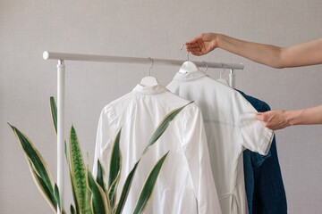 a woman's hand holding clothes on a hanger, a rail or Wardrobe in the living room, a stylist or fashion blogger sorting closet, sorting clothes for life and recycling, large closet to store things and