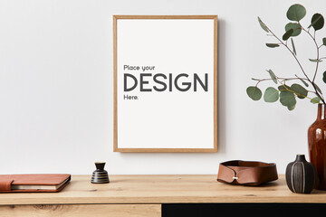 Stylish interior of living room with mock up poster frame, wooden commode, book, eucalyptus leaf in...
