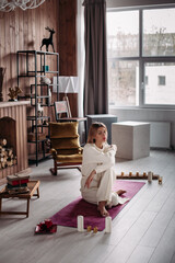 Beautiful young girl wearing natural organic eco-friendly white cotton sportswear, sitting on mat in cozy home interior