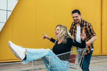 Young beautiful couple riding in a a supermarket shopping cart and having fun
